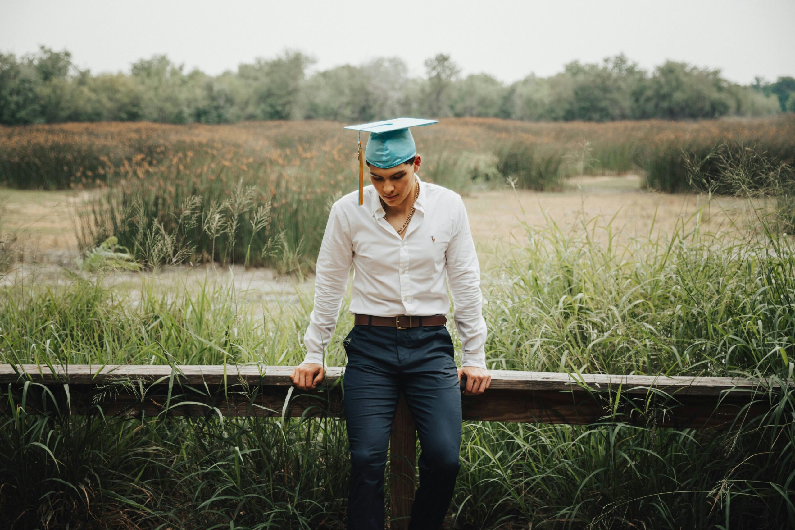 Man in White Shirt and Academic Hat Sitting in Countryside